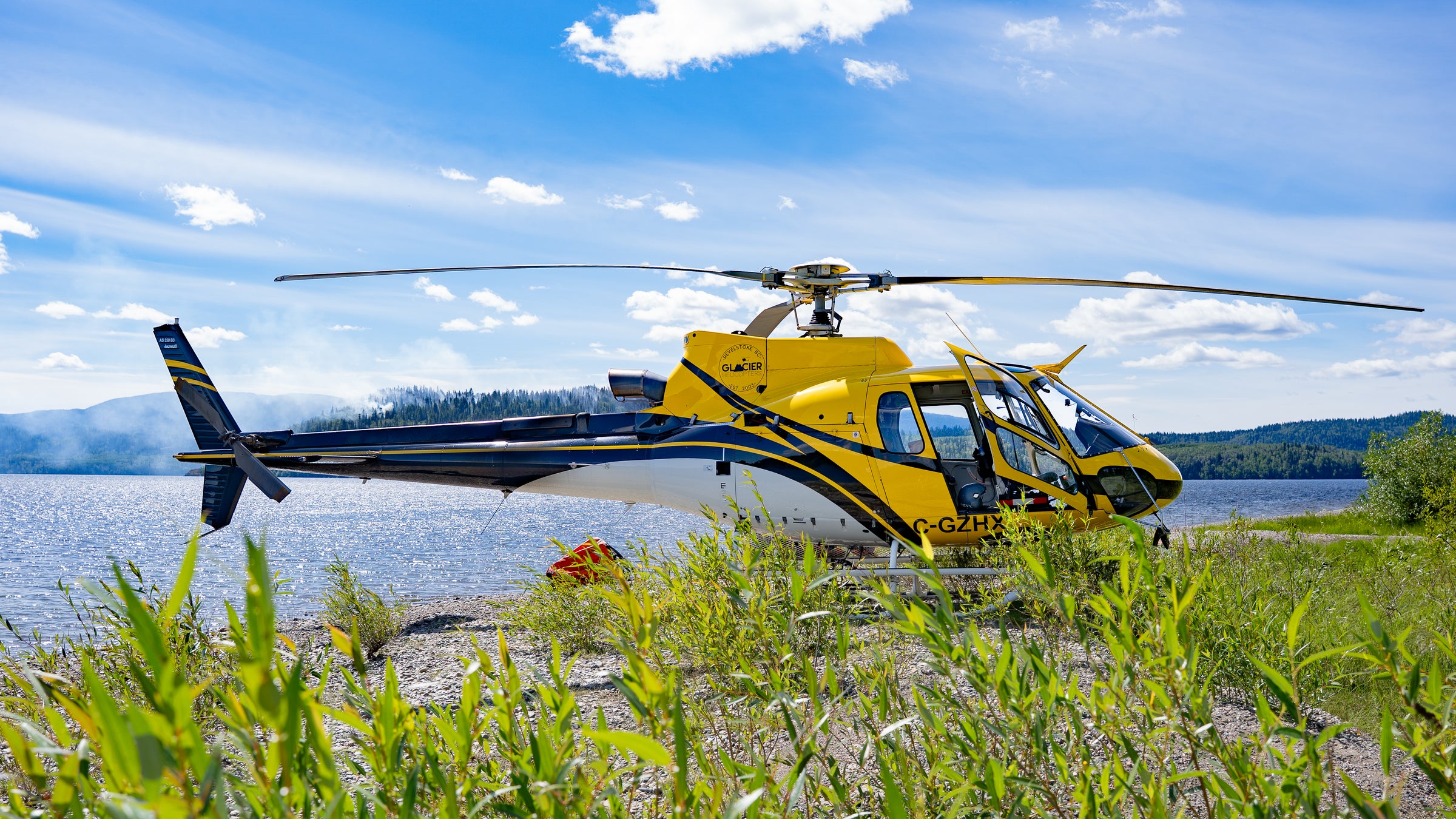 Helicopter flying over a scenic landscape with water and mountains in the background.